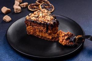 A piece of fresh delicious cake with nuts and chocolate on a black plate against a dark blue background photo