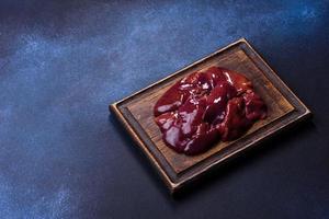 Pieces of raw liver on a wooden cutting board against a dark concrete background photo