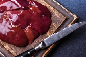 Pieces of raw liver on a wooden cutting board against a dark concrete background photo