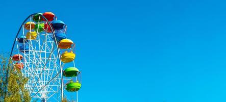 landscape of an amusement park with the top of a Ferris wheel showing above the tree tops against a blue sky. photo