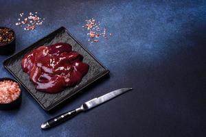 Pieces of raw liver on a wooden cutting board against a dark concrete background photo