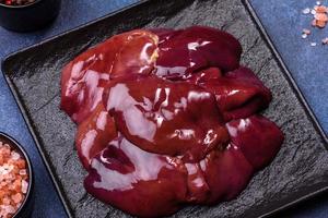 Pieces of raw liver on a wooden cutting board against a dark concrete background photo