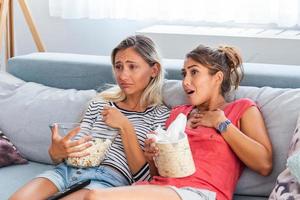 Two sentimental women friends upset crying and wiping tears with handkerchiefs while watching dramatic, sad movie, TV reality show or touching old home video on laptop while sitting on sofa at home photo