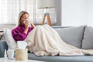 mujer enferma con dolor de cabeza sentada debajo de la manta. mujer enferma con infecciones estacionales, gripe, alergia acostada en la cama. mujer enferma cubierta con una manta acostada en la cama con fiebre alta y gripe, descansando. foto