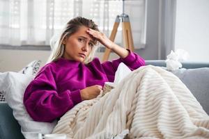mujer enferma con dolor de cabeza sentada debajo de la manta. mujer enferma con infecciones estacionales, gripe, alergia acostada en la cama. mujer enferma cubierta con una manta acostada en la cama con fiebre alta y gripe, descansando.