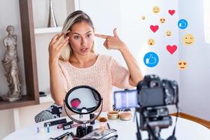 Famous blogger. Cheerful female vlogger is showing cosmetics products while recording video and giving advices for her beauty blog. Focus on digital camera photo