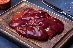 Pieces of raw liver on a wooden cutting board against a dark concrete background photo