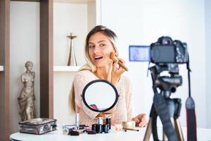 blogger famoso. una alegre bloguera muestra productos cosméticos mientras graba videos y da consejos para su blog de belleza. centrarse en la cámara digital foto