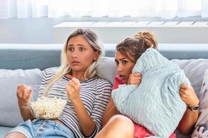 Terrified friends watching tv in the night sitting on a couch in the living room at home. Scary Movie Night with Girlfriends, Frightened young women watching scary movie at home. photo