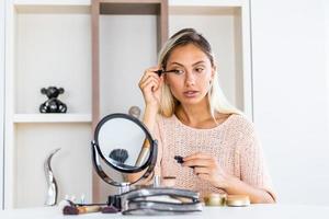 Beautiful woman applying make up paint her eyelashes for a evening date in front of a mirror. photo