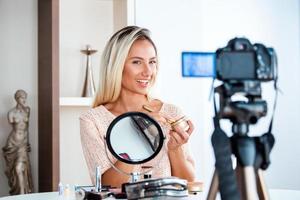 Famous blogger. Cheerful female vlogger is showing cosmetics products while recording video and giving advices for her beauty blog. Focus on digital camera photo