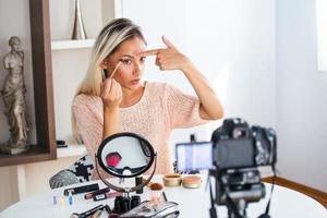 Famous blogger. Cheerful female vlogger is showing cosmetics products while recording video and giving advices for her beauty blog. Focus on digital camera photo