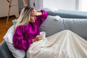 Sick woman with headache sitting under the blanket. Sick woman with seasonal infections, flu, allergy lying in bed. Sick woman covered with a blanket lying in bed with high fever and a flu, resting. photo