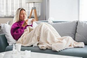 Sick woman with headache sitting under the blanket. Sick woman with seasonal infections, flu, allergy lying in bed. Sick woman covered with a blanket lying in bed with high fever and a flu, resting. photo