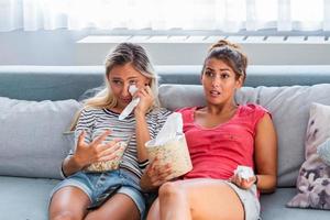 Two sentimental women friends upset crying and wiping tears with handkerchiefs while watching dramatic, sad movie, TV reality show or touching old home video on laptop while sitting on sofa at home photo