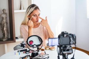 Famous blogger. Cheerful female vlogger is showing cosmetics products while recording video and giving advices for her beauty blog. Focus on digital camera photo