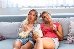 two best friends watch sad movie at home in bed crying touching. girls hold popcorn and tv remote control looking screen romantic film on television. ladies in pajama wiping tear using tissue photo