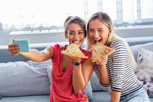 amigos comiendo pizza y sonriendo para selfie. están compartiendo pizza y hacen una foto selfie en un teléfono inteligente.