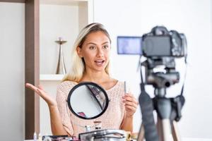Famous blogger. Cheerful female vlogger is showing cosmetics products while recording video and giving advices for her beauty blog. Focus on digital camera photo