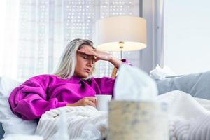 Sick Woman.Flu.Woman Caught Cold. Sneezing into Tissue. Headache. Virus .Medicines. Young Woman Infected With Cold Blowing Her Nose In Handkerchief. Sick woman with a headache sitting on a sofa photo