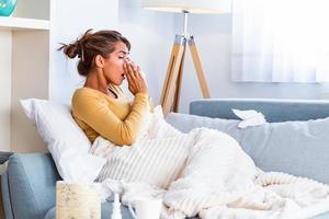 Sick day at home. Young woman has runny and common cold. Cough. Closeup Of Beautiful Young Woman Caught Cold Or Flu Illness. Portrait Of Unhealthy Girl blowing her nose photo