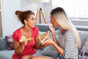 Friendship, food and leisure concept - Two happy female friends eating pizza and drinking wine at home. Girlfriends having fun photo