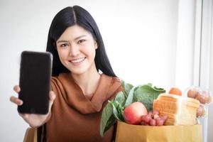 hermosa mujer asiática sosteniendo un teléfono inteligente, pidiendo comida en línea. el concepto de negocio de los servicios de entrega de alimentos durante el coronavirus. copie el espacio foto