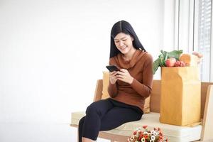 Beautiful smiling Asian woman holding a smartphone to order food online. The business concept of food delivery services during the coronavirus. Copy space photo