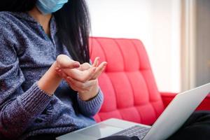 una mujer asiática que usa una máscara trabaja en casa durante el coronavirus masajea los dedos para deshacerse del dolor. porque ella trabaja todo el día. el concepto de distancia social. problemas de salud síndrome de oficina foto