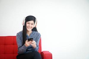 A beautiful smiling young woman holding a smartphone and wearing headphones to music Sit on the sofa in the house. Concept of rest on vacation. Social distance during the coronavirus. copy space photo