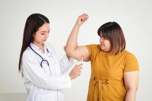 las doctoras usan el calibrador de grasa para medir la grasa en los brazos de las mujeres obesas, ayudándolas en su plan de pérdida de peso. Fondo blanco. el concepto de mantener una buena salud foto