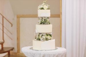 Wedding cake. Close-up photo of a beautiful white three-tiered wedding cake decorated by flowers and greenery