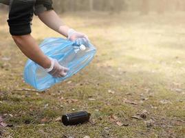 Young man collects trash plastic, glass from the ground. A volunteer cleans up the park on a sunny bright day. Clearing, pollution, ecology and plastic concept photo