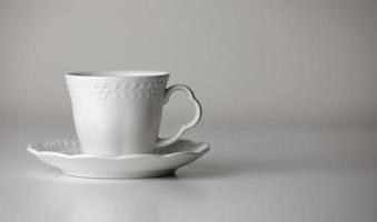 White tea cup and saucer with a pattern for drink on white background. Ceramic coffee cup or mug close up. Mockup classic porcelain utensils. copy space photo