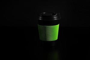 a glass of hot tea or coffee. Black paper glass with a lid on a black background. side view photo