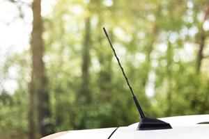 bosque verde detrás de la antena del automóvil. antena del automóvil para recibir las ondas de radio en el techo del automóvil. enfoque selectivo y primer plano foto