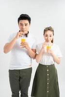 Stylish couple in casual clothes is drinking juice, looking at camera and smiling on white background photo