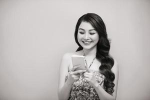 retrato de una mujer casual sonriente sosteniendo un teléfono inteligente sobre fondo blanco. foto en blanco y negro.