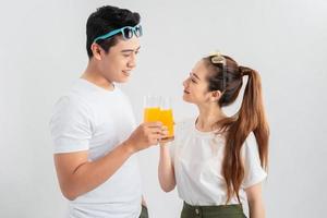 hermosa pareja joven de pie aislada sobre fondo blanco, sosteniendo vasos con jugo de naranja foto