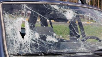 Löcher in der Windschutzscheibe des Autos, es wurde aus einer Schusswaffe geschossen. Einschusslöcher. Windschutzscheibe zerschlagen, kaputtes und beschädigtes Auto. Die Kugel hinterließ ein zerbrochenes Loch im Glas. video