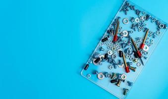 Top view metal bolts, nuts, washer, and screw in a plastic tray on blue background. Fasteners equipment. Hardware tools of mechanics technicians. Threaded fastener accessories. Hardware nuts and bolts photo