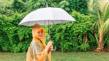 Asian boy puts on a raincoat and opens an umbrella on a rainy day. photo