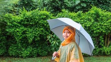 Asian boy puts on a raincoat and opens an umbrella on a rainy day. photo