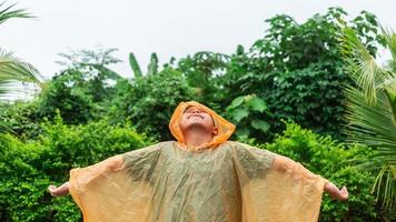 un niño asiático con impermeable naranja es feliz y se divierte bajo la lluvia en un día lluvioso. foto