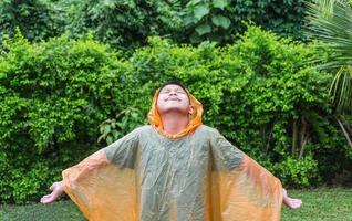 un niño asiático con impermeable naranja es feliz y se divierte bajo la lluvia en un día lluvioso. foto