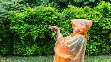 un niño asiático con impermeable naranja es feliz y se divierte bajo la lluvia en un día lluvioso. foto