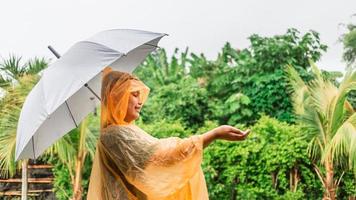 Asian boy wearing orange raincoat holding umbrella happy and having fun in the rain on a rainy day photo