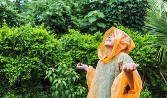 un niño asiático con impermeable naranja es feliz y se divierte bajo la lluvia en un día lluvioso. foto