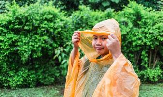 un niño asiático con impermeable naranja es feliz y se divierte bajo la lluvia en un día lluvioso. foto