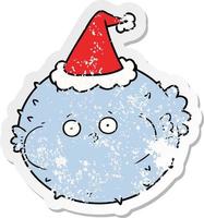 distressed sticker cartoon of a puffer fish wearing santa hat vector